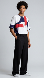 A man modeling a short-sleeve crewneck t-shirt with a bold geometric color-block pattern in white, navy, and red, paired with black wide-leg trousers and white sneakers, against a light gray studio background.