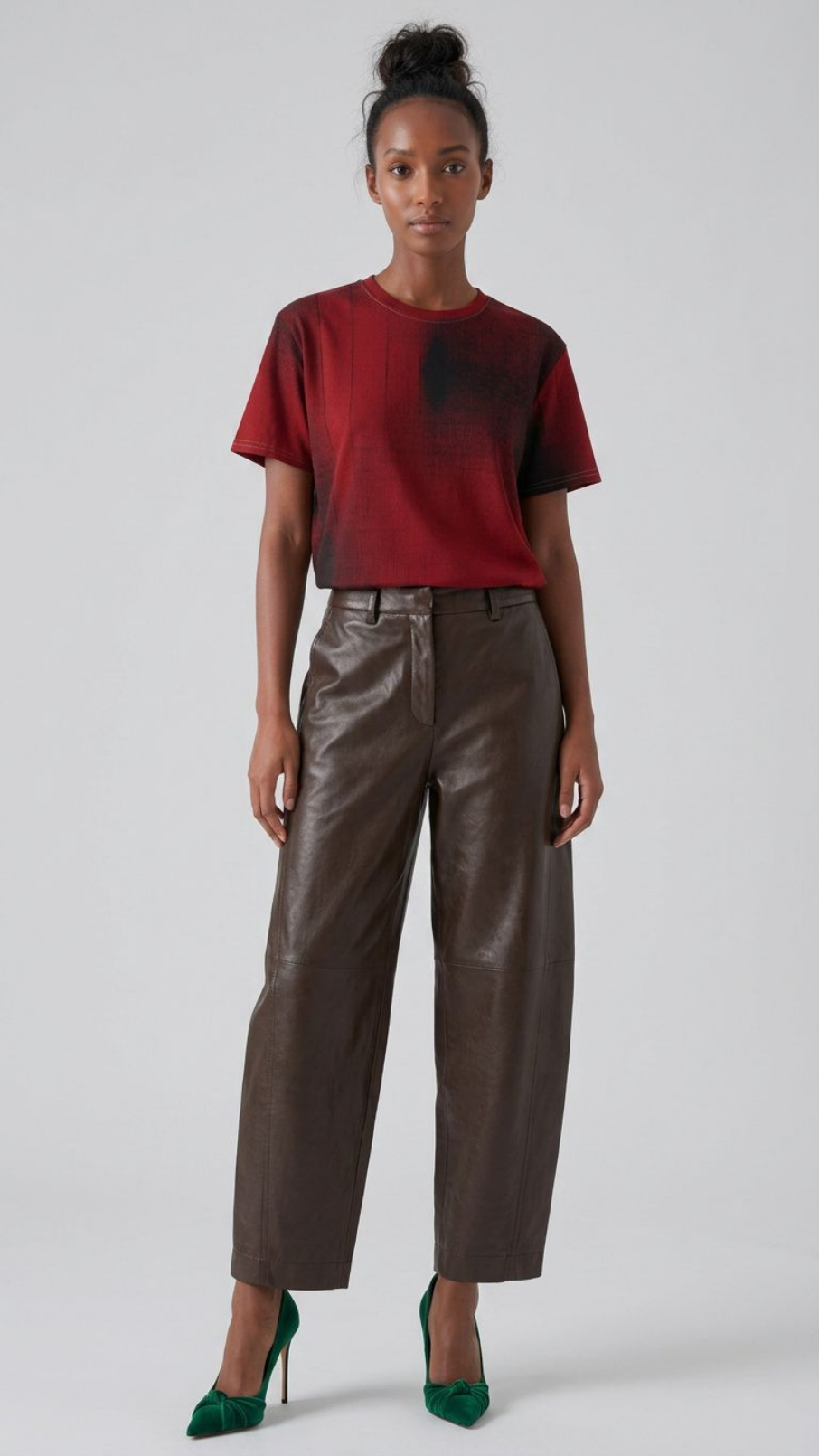 A model stands against a light gray studio background wearing a short-sleeve crewneck t-shirt with a red-to-black gradient, brown wide-leg faux-leather cropped pants, and green high heels.